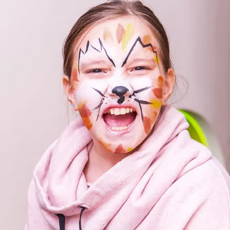 Smiling girl with colorful cat face paint wearing a pink hoodie at a party